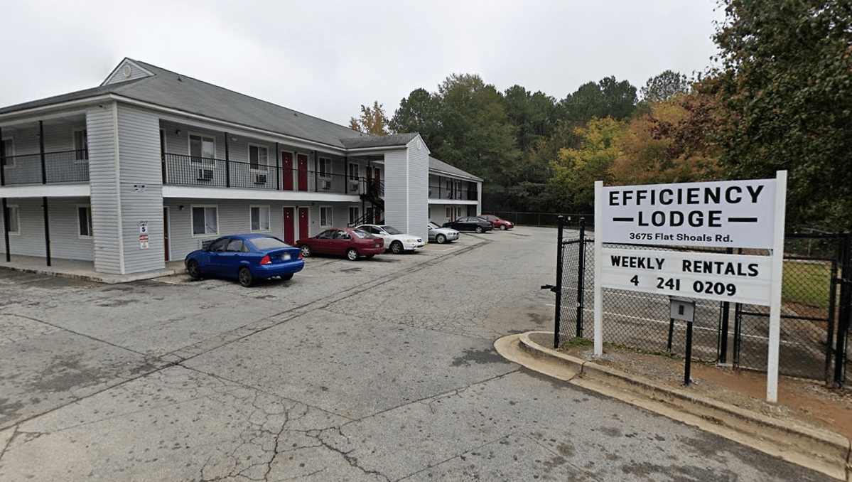 A grey, low-rise hotel complex is fronted by a sign reading "Efficiency Lodge."