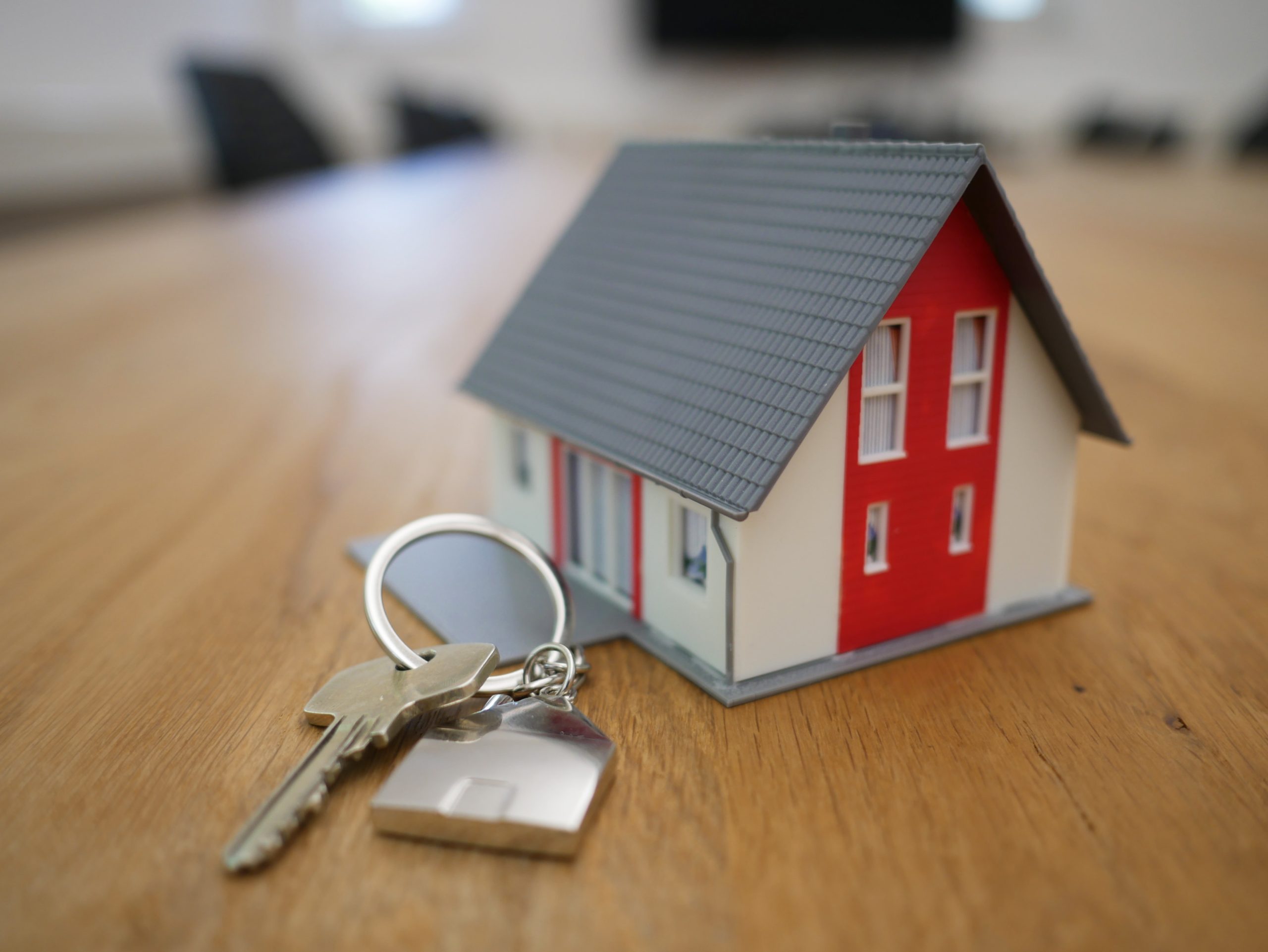 A miniature house sits on a wooden table with a set of keys.