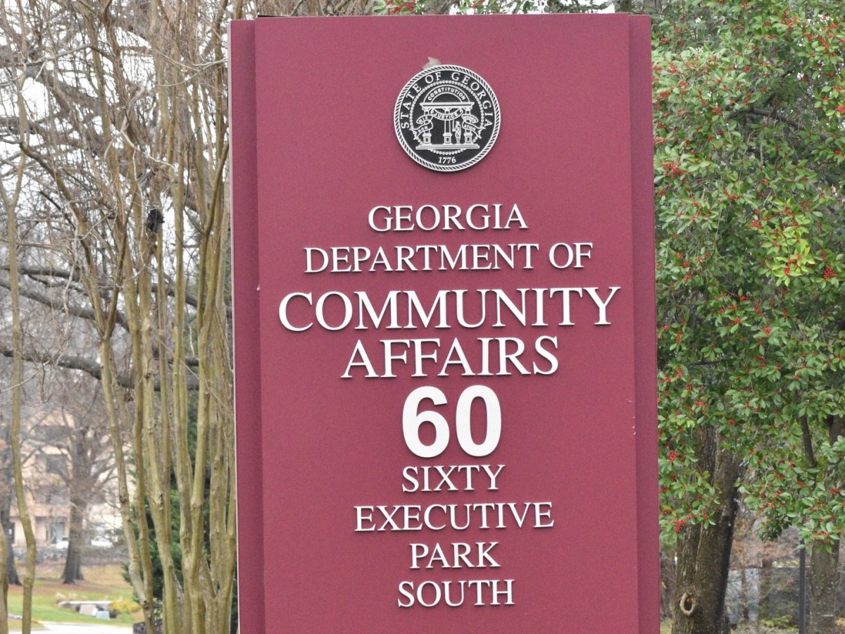 A pale red sign with a government insignia stands outside the Georgia Department of Community Affairs office.