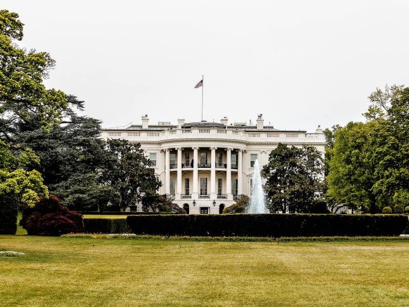 A photo of the White House, surrounded by trees and a sprawling green lawn.