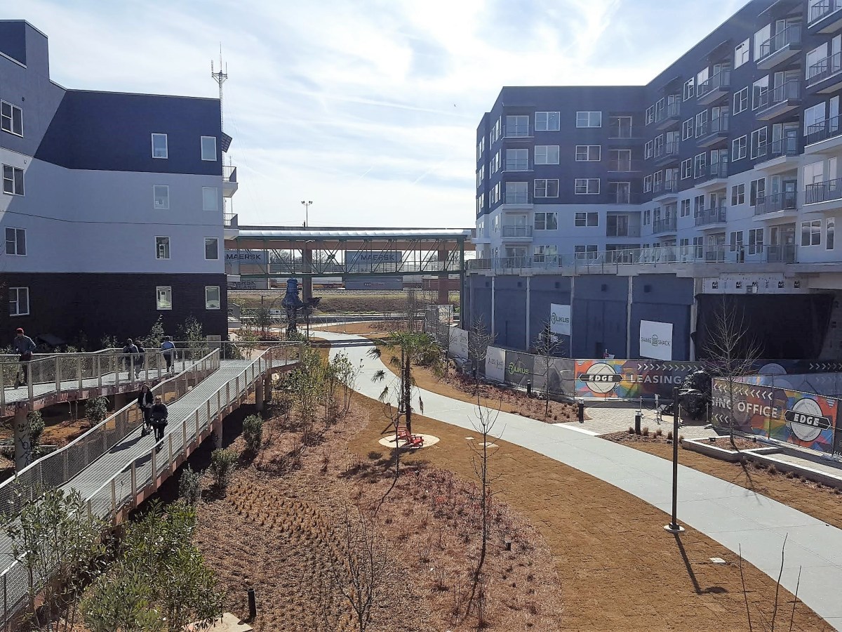 A photo of a blue and white apartment complex split into two buildings with a skybridge connecting them over the Beltline trail.