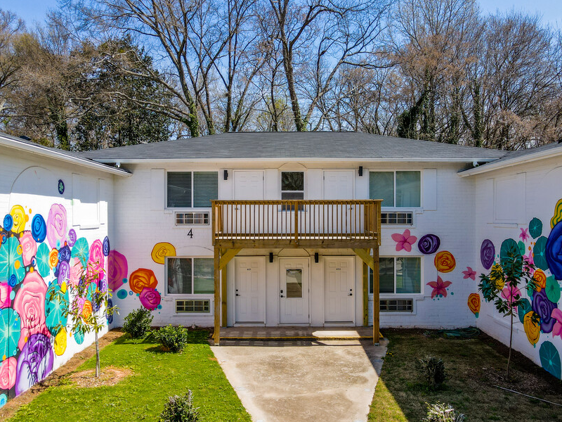 A low-rise, U-shaped apartment complex is painted white with colorful murals on its sides.