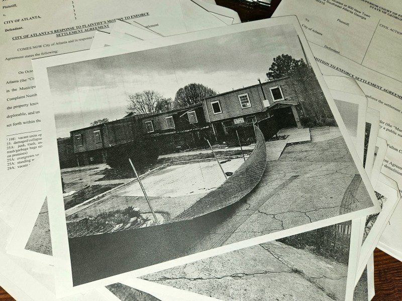 A photo of a stack of court documents from the Forest Cove case, including a photograph of the complex, which shows a fence torn down and buildings falling apart.