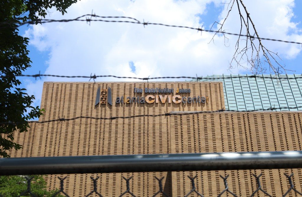 A photograph of the brick Atlanta Civic Center, as seen from behind a chain-link fence with barbed wire at the top.