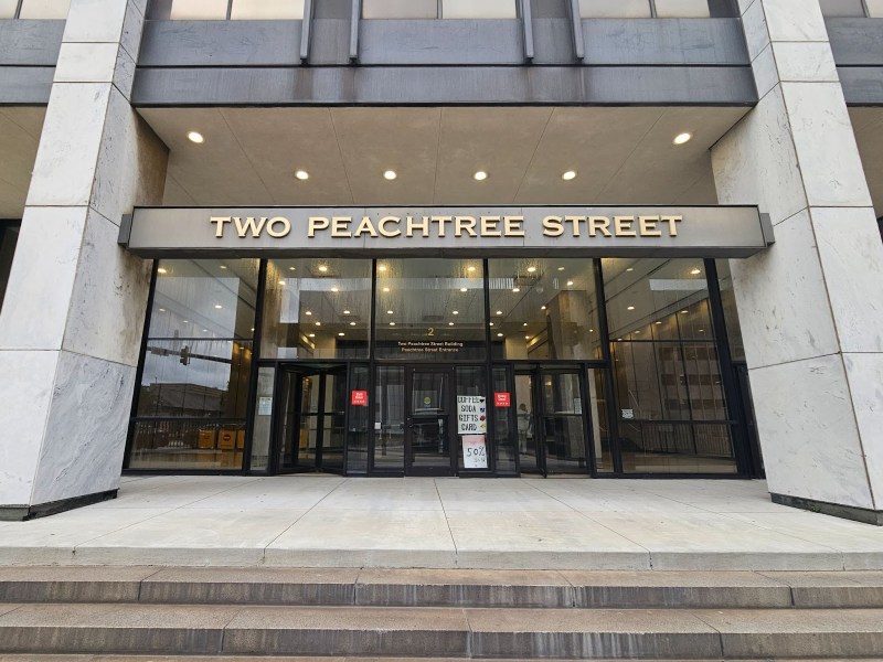 A photo of the front entrance to the 2 Peachtree tower, with gold lettering spelling out the building's name above glass doors.
