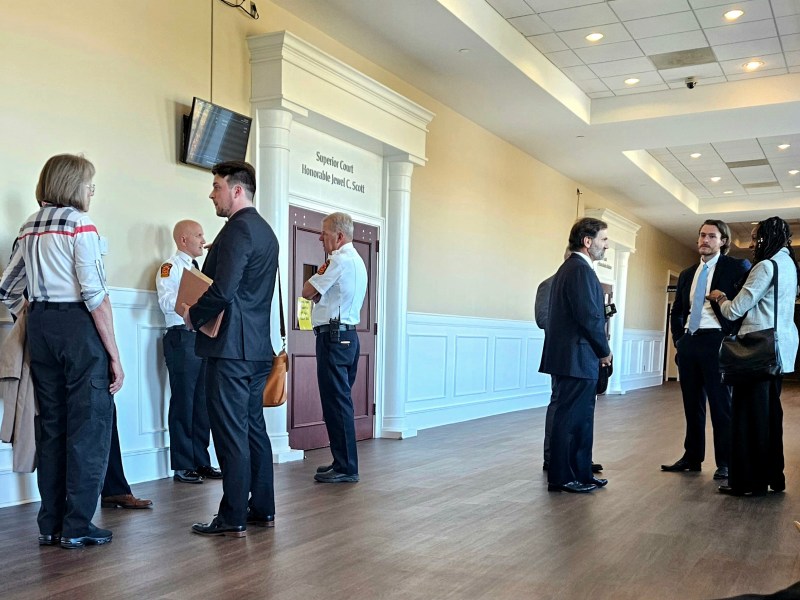 A group of attorneys in suits and fire officials in uniform stand outside of a courtroom.