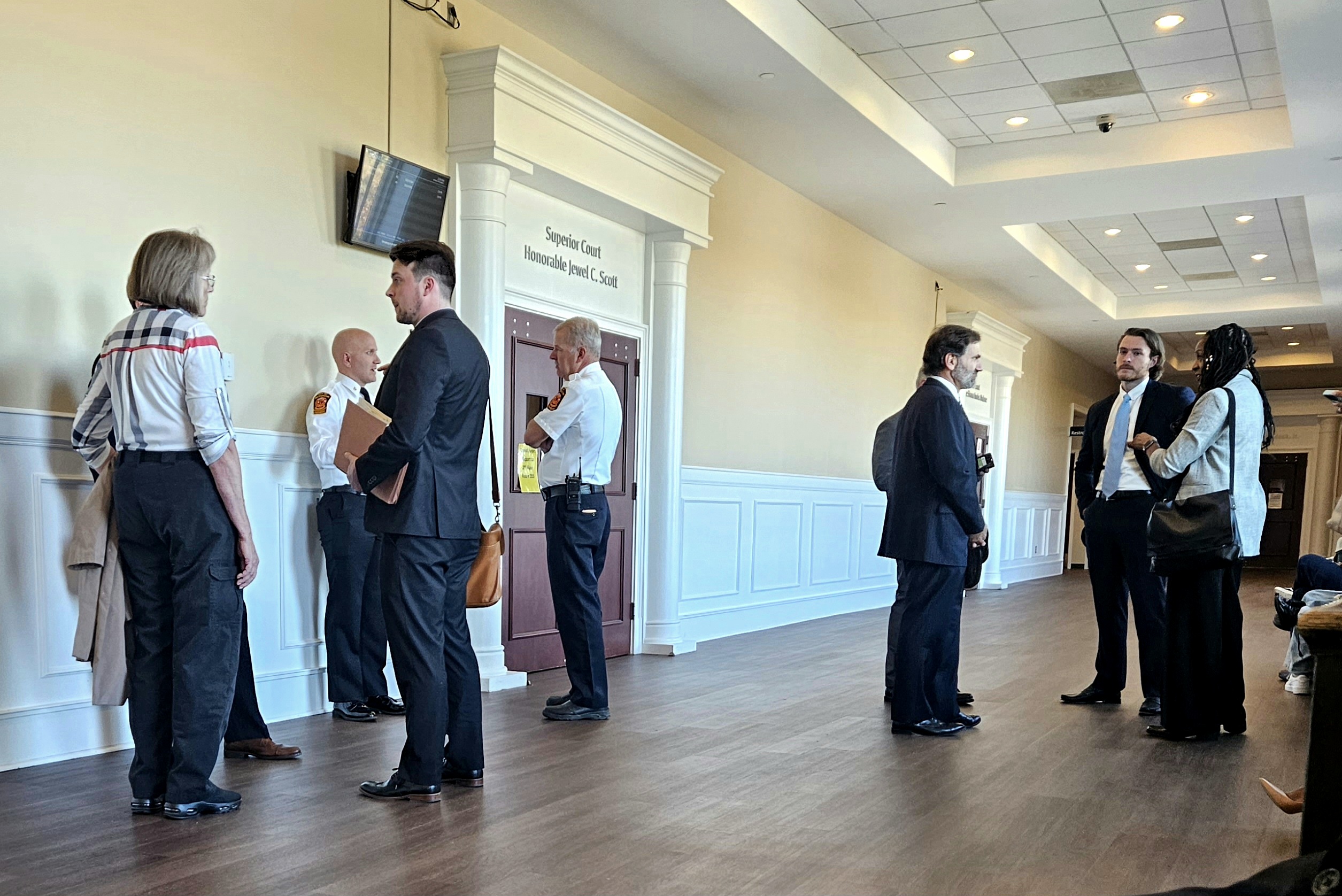 A group of attorneys in suits and fire officials in uniform stand outside of a courtroom.