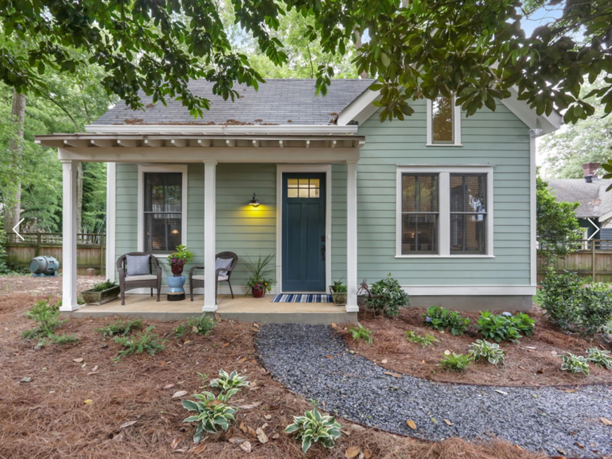 A photo of a small, pale-blue home shaded by trees.