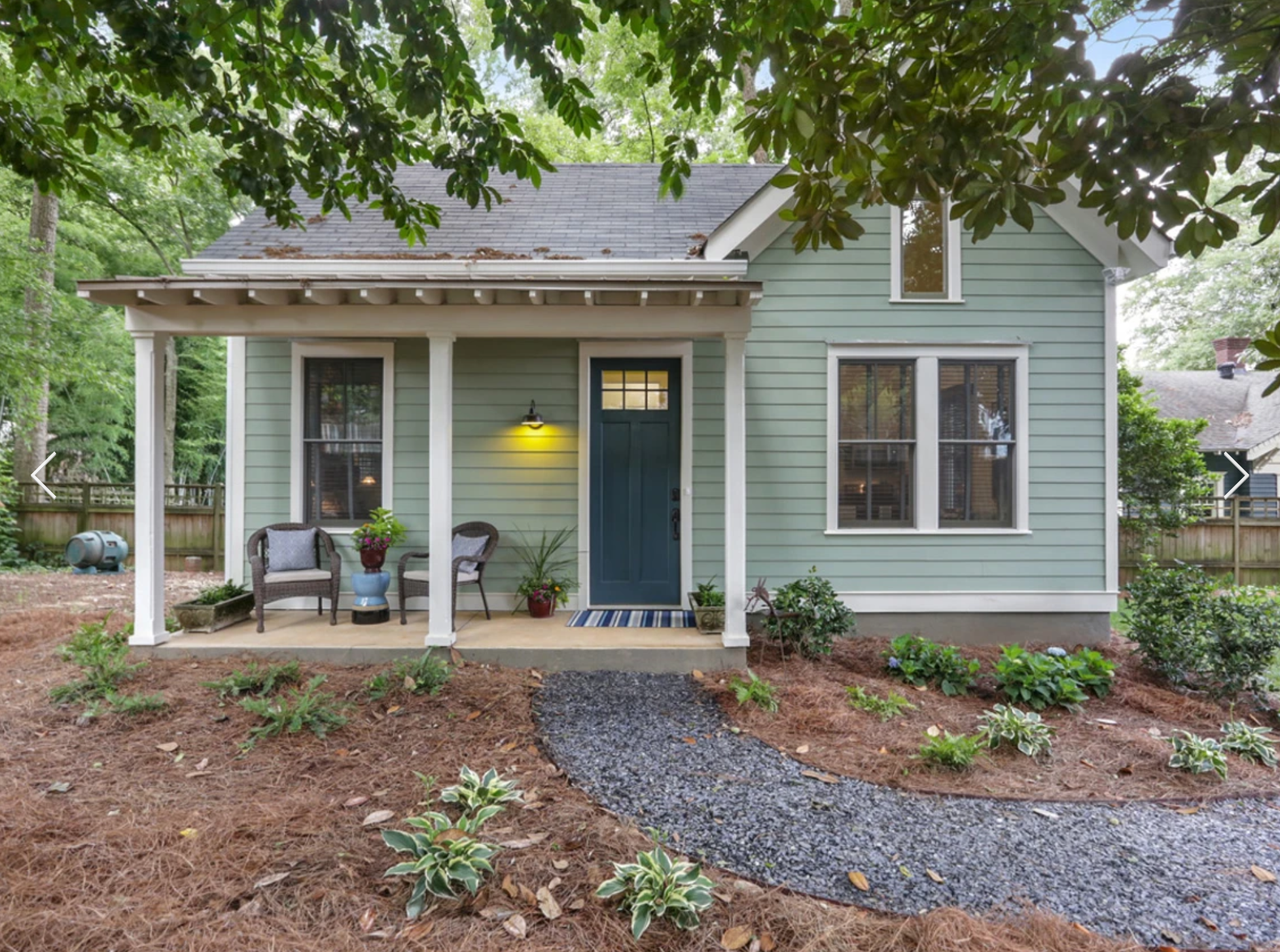 A photo of a small, pale-blue home shaded by trees.