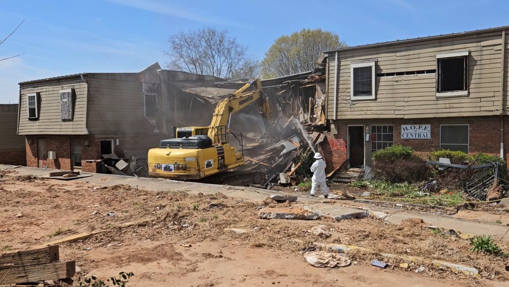 A photo of an excavator tearing down a low-rise apartment complex.