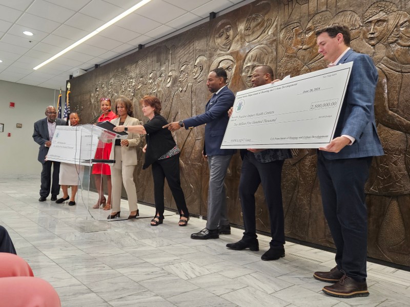 HUD and city officials and nonprofit leaders present two oversize checks representing federal funds going toward housing initiatives.