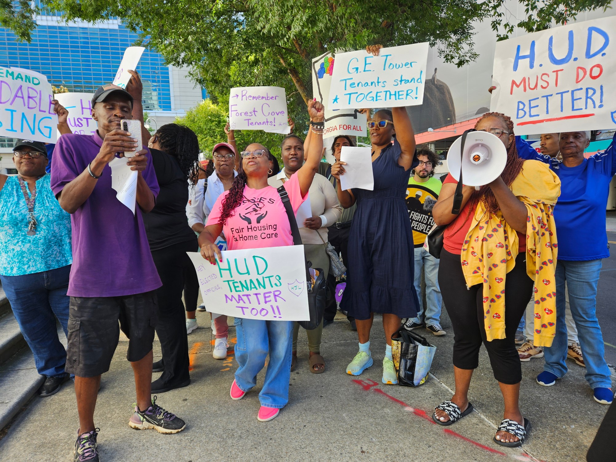 A photo of protesters toting picket signs reading things like, "HUD MUST DO BETTER."