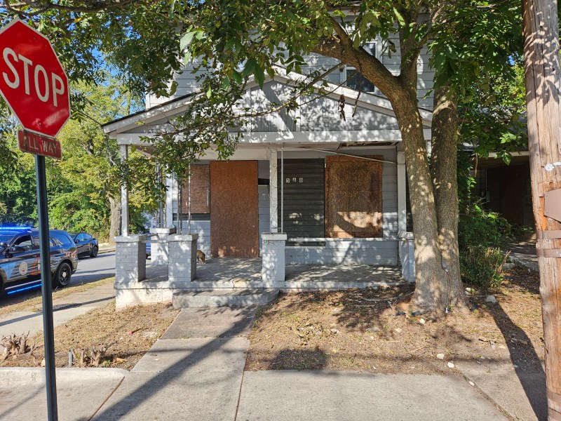 A photo of a boarded-up house with weeds sprouting around it.