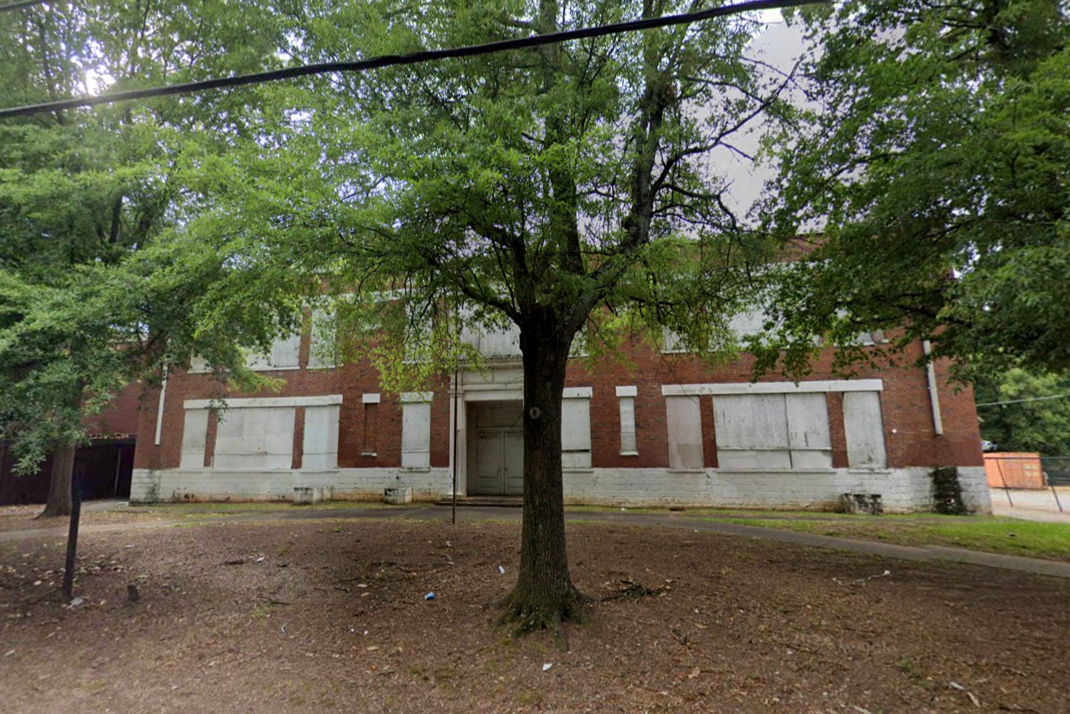 A photo of an old brick schoolhouse surrounded by trees.