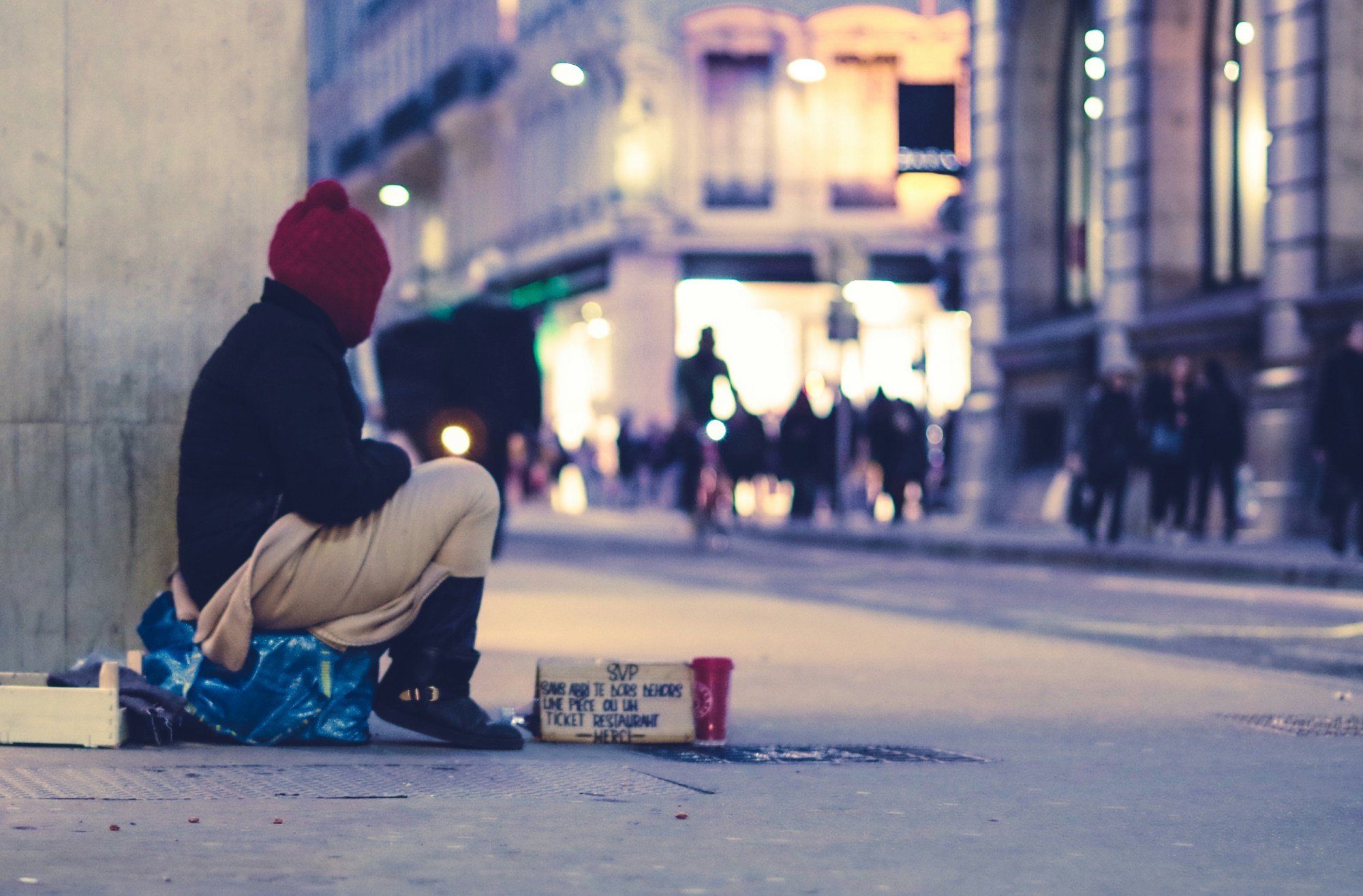 A photo of a young person sitting on the street near a sign asking for help.