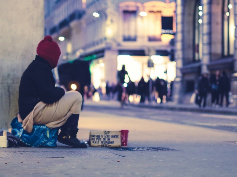 A photo of a young person sitting on the street near a sign asking for help.