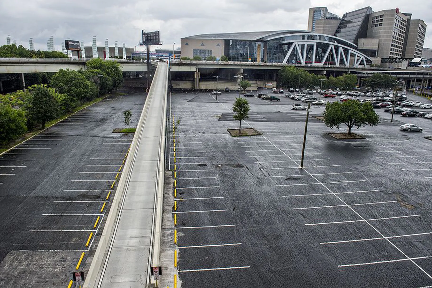 A photo of a rain-soaked parking lot, bisected by a ramp that leads to an overhead bridge.