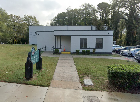 A photo of a rectangular white building with a green sign out front.
