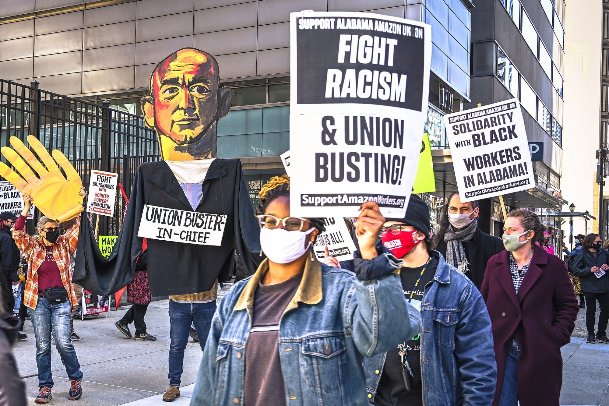 Amazon workers in Alabama hold a labor action in the street holding a sign that says "Fight Racism & Union Busting"