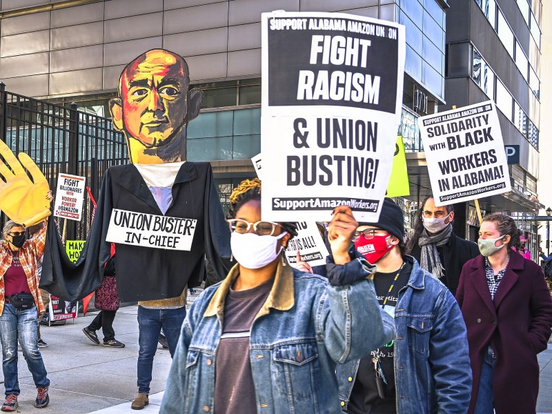 Amazon workers in Alabama hold a labor action in the street holding a sign that says "Fight Racism & Union Busting"