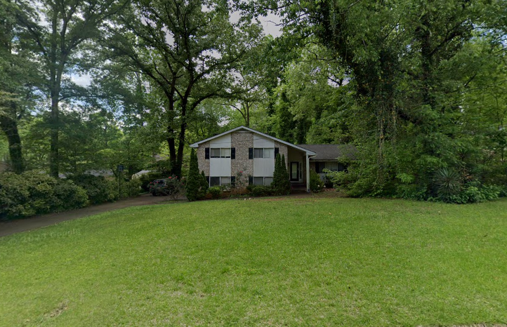 A photo of a small grey house surrounded by trees.