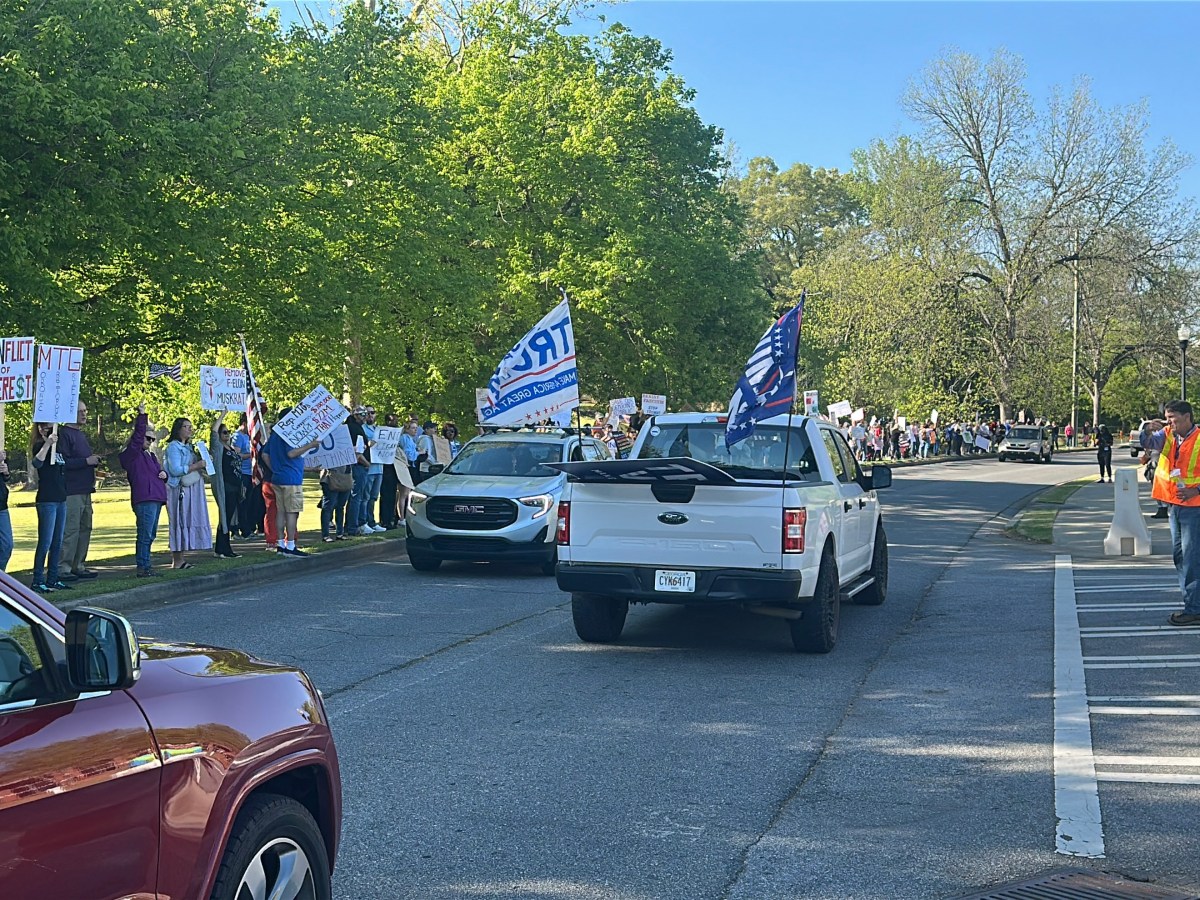 A white pickup truck with Trump flags drives by a line of protestors outside the Acworth Community Center where Congresswoman Marjorie Taylor Greene held a Town Hall on April 15, 2025.