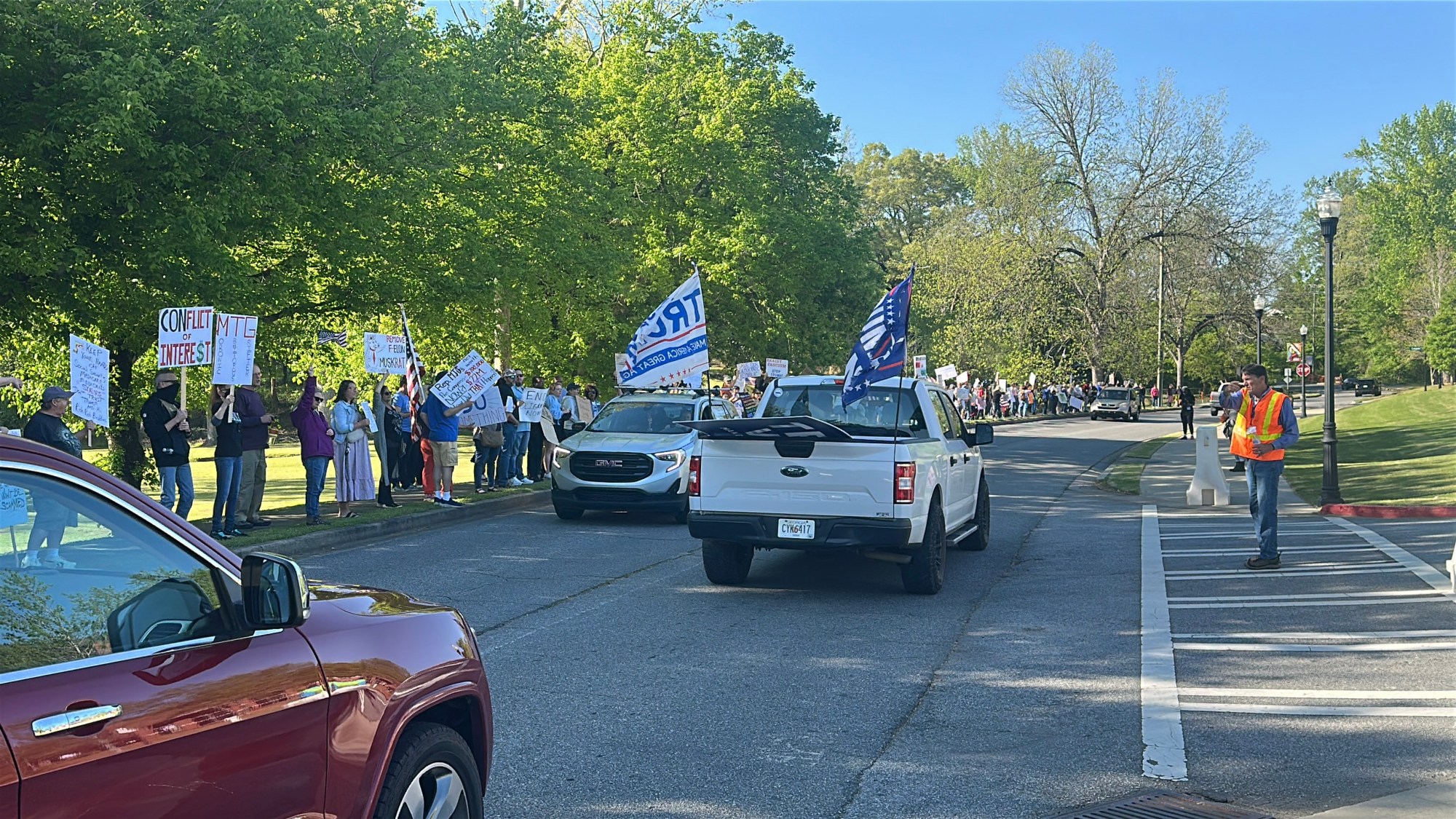 A white pickup truck with Trump flags drives by a line of protestors outside the Acworth Community Center where Congresswoman Marjorie Taylor Greene held a Town Hall on April 15, 2025.