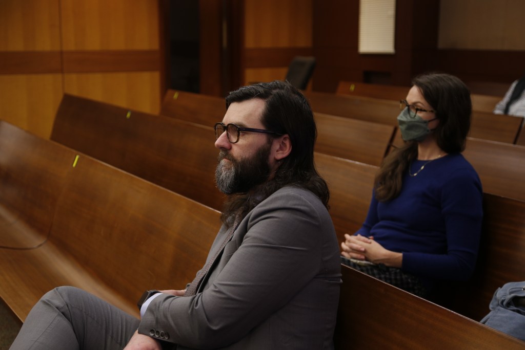 Matt Scott, center, has long black hair and a greying bear. He wears a grey suit.