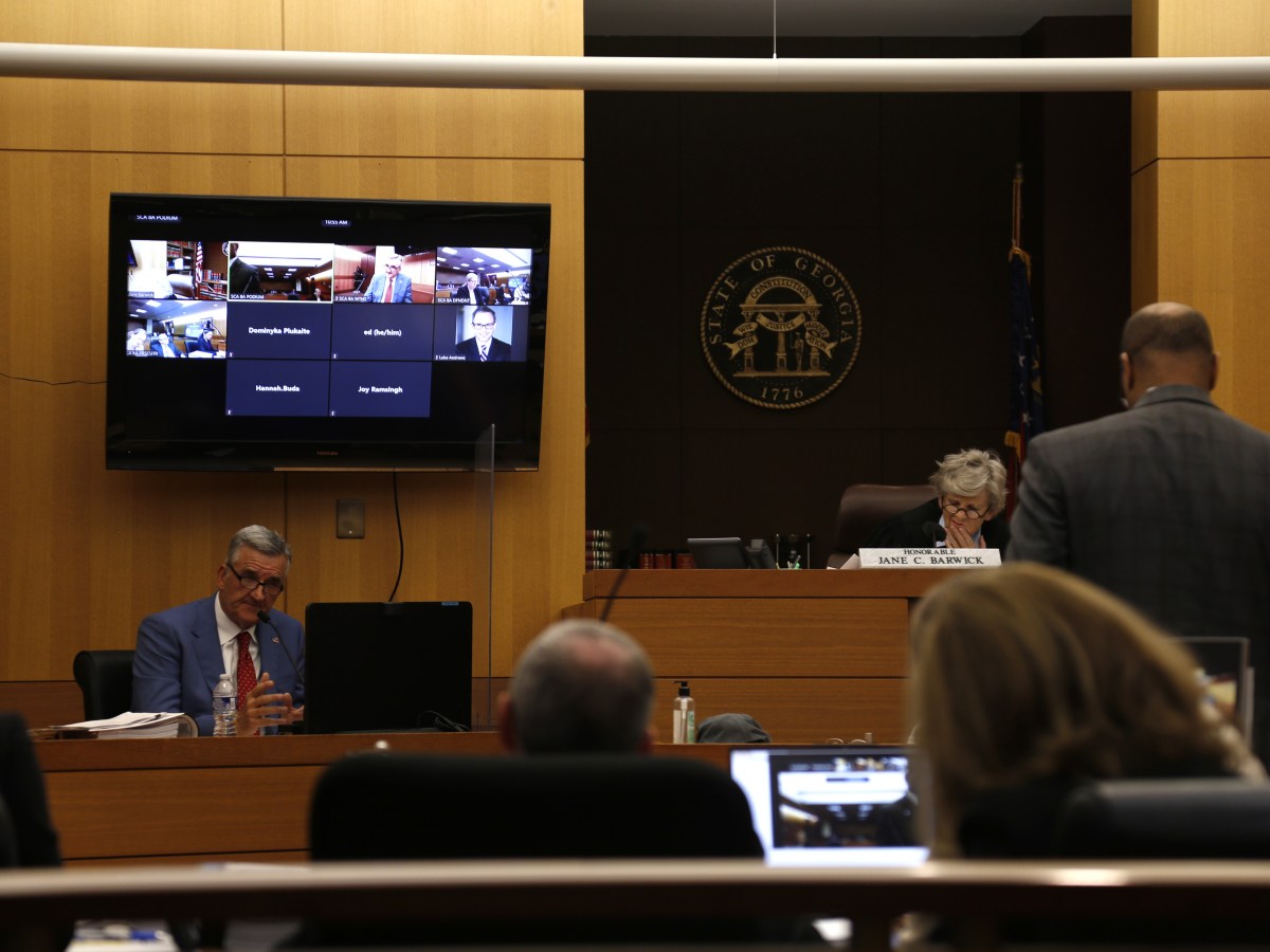 Dave Wilkinson, a grey-haired white man in a blue-grey suit, testifies on the stand. To his right is white-haired Fulton Judge Jane Barwick, wearing a black robe. The courtroom is wood-paneled.