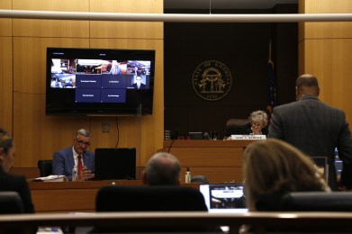 Dave Wilkinson, a grey-haired white man in a blue-grey suit, testifies on the stand. To his right is white-haired Fulton Judge Jane Barwick, wearing a black robe. The courtroom is wood-paneled.