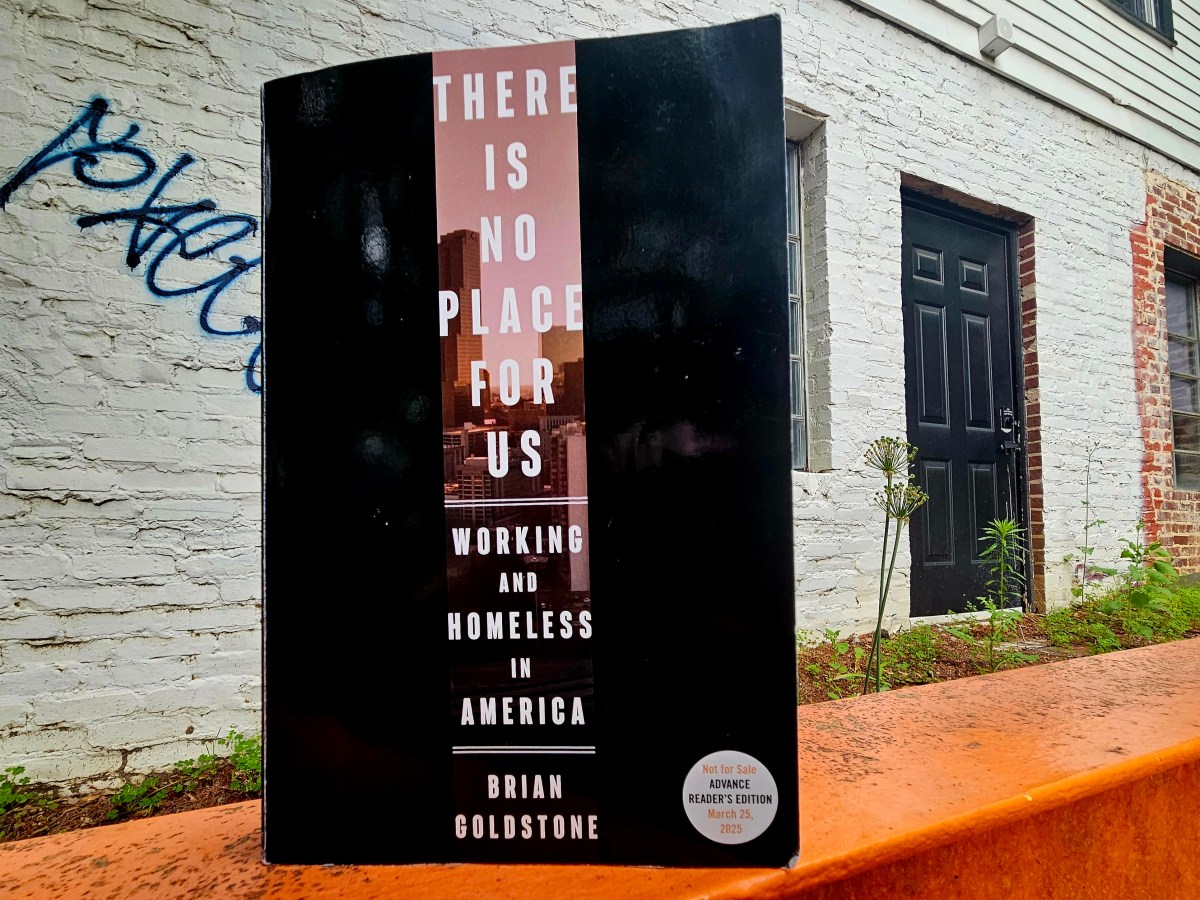 A photo of the book "There Is No Place For Us," stood in front of a spray-painted building