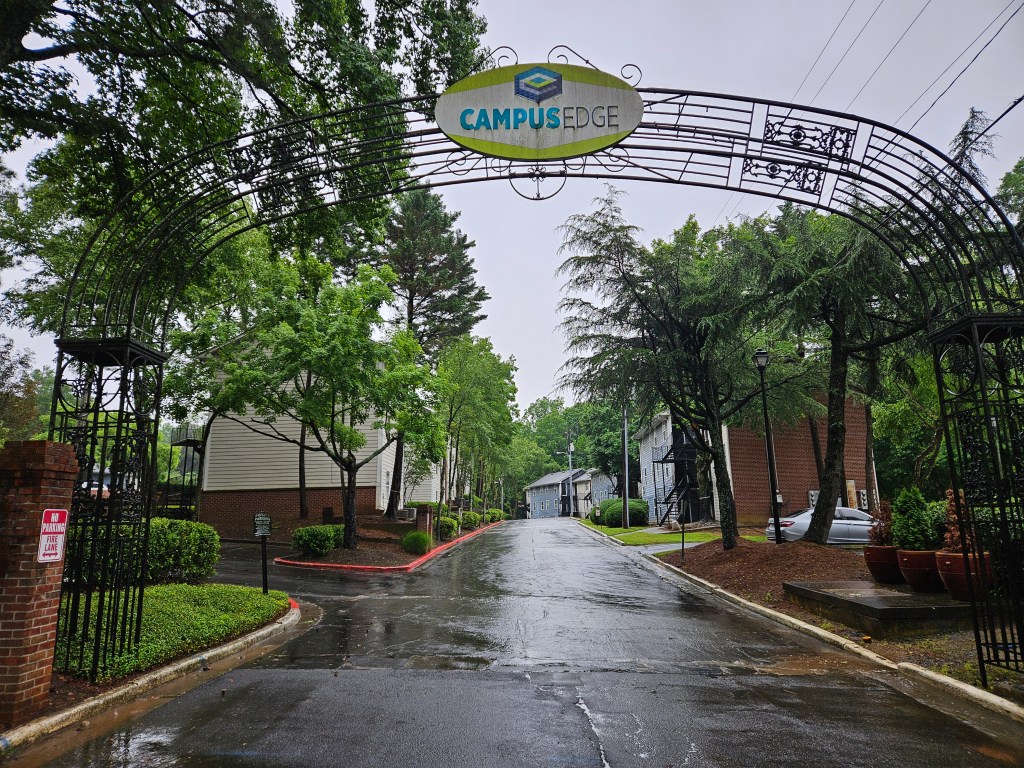 An archway with a sign reading "Campus Edge" leads into a mid-rise apartment complex.