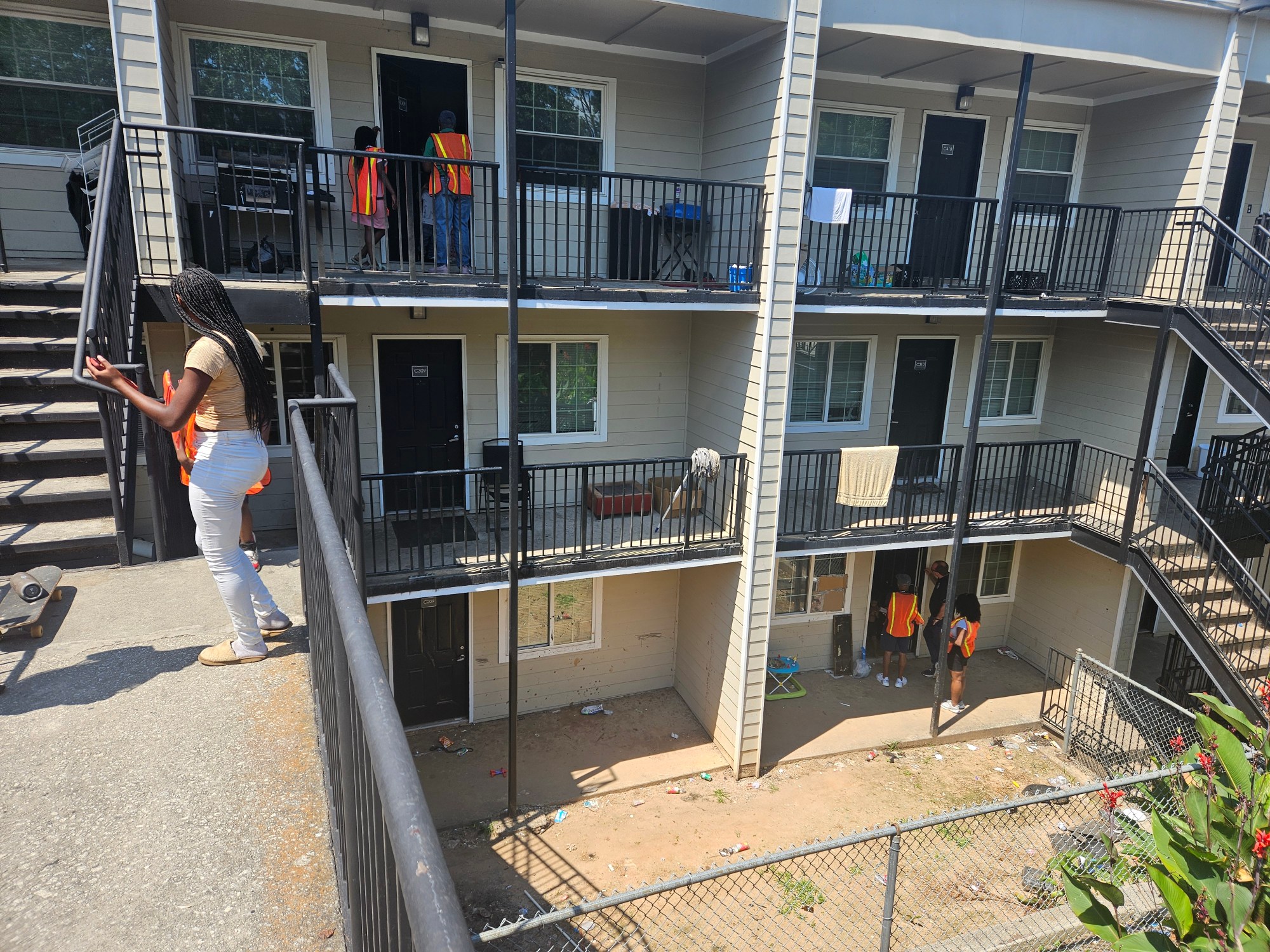 A photo of a three-story apartment complex. Activists in orange reflective vests knock on doors.