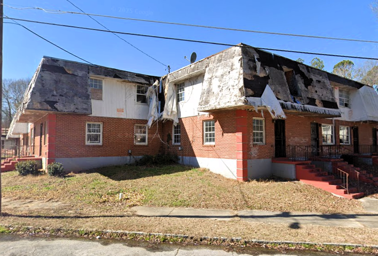A photo of a low-rise apartment complex with holes in the side from fire and neglect.