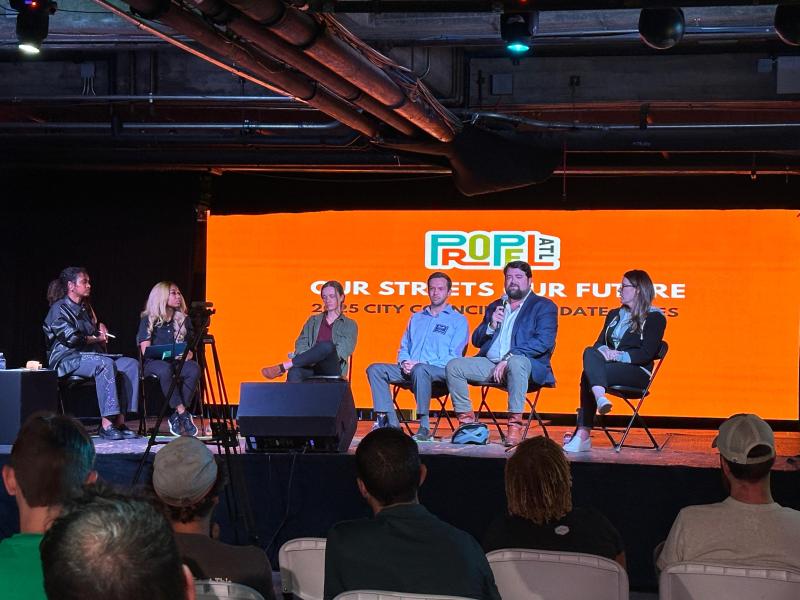 A photo of six people sitting in folding chairs on a stage.