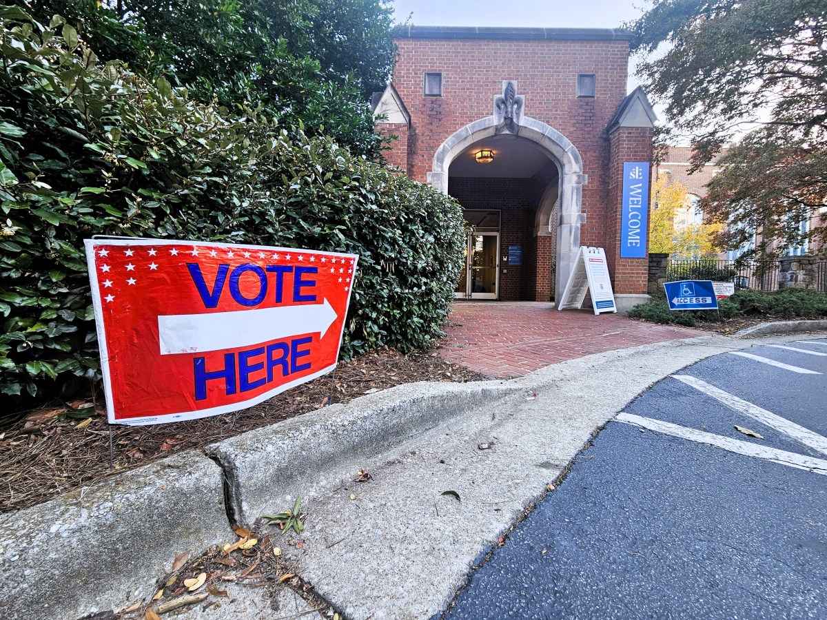 A photo of a red sign reading "VOTE HERE" in front of the entrance to a church.
