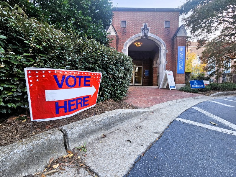 A photo of a red sign reading "VOTE HERE" in front of the entrance to a church.