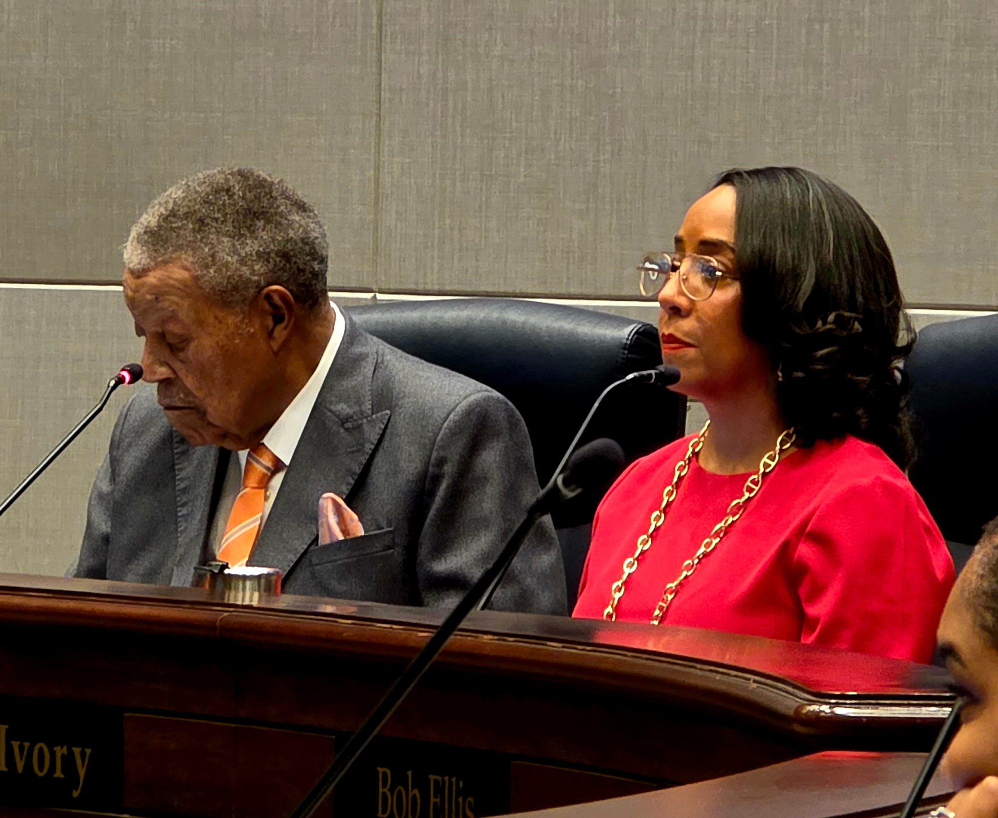 A photograph of Fulton Chair Robb Pitts in a grey suit, seated next to County Commissioner Mo Ivory, in a pink blouse and glasses.