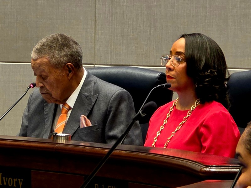 A photograph of Fulton Chair Robb Pitts in a grey suit, seated next to County Commissioner Mo Ivory, in a pink blouse and glasses.